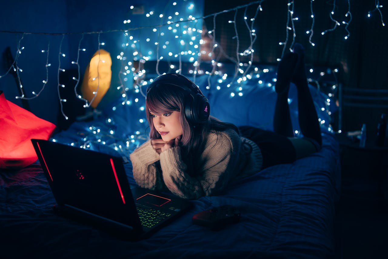 services-01 A young woman in a cozy room, wearing headphones and using a laptop, surrounded by warm fairy lights.