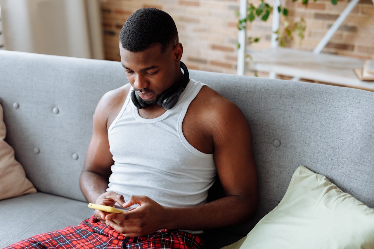 services-04 A young man in casual attire using a smartphone while relaxing indoors.